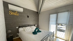 Une chambre avec un lit, un climatiseur fixé au mur, un panneau avec le mot «
Smile
» (Sourire), une lampe et une fenêtre avec des stores.