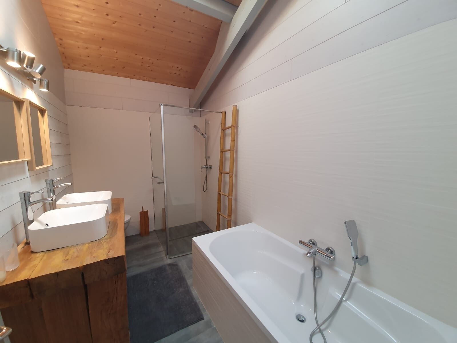 A modern bathroom with a wooden ceiling, a large bathtub, a glass shower enclosure, and a wooden vanity with a sink.