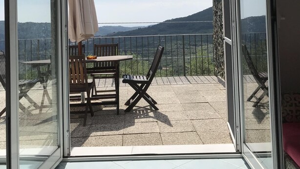 Un balcon avec une table et des chaises, un parasol et une vue sur la campagne.