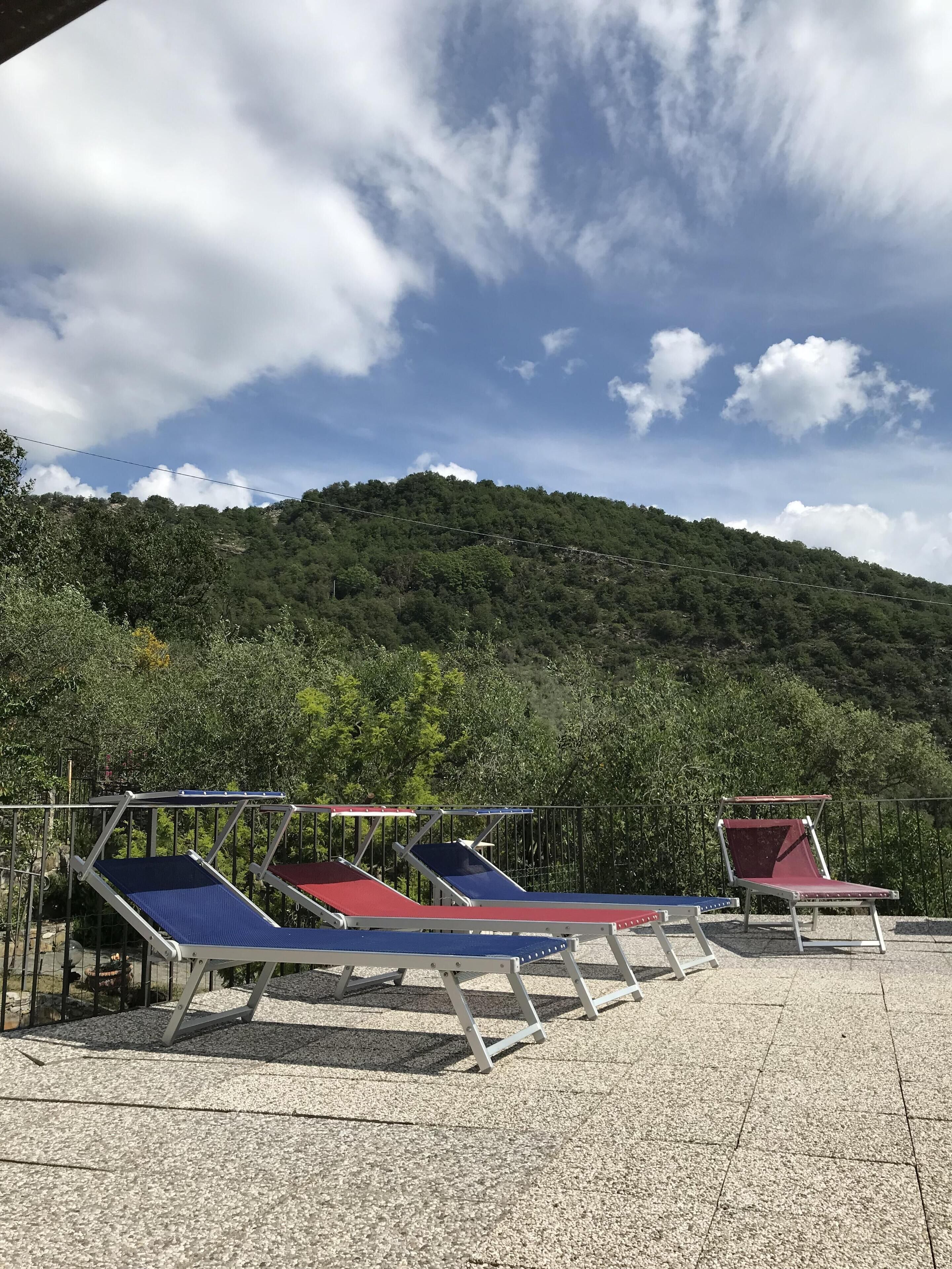 A terrace with sun loungers and a view of a forested hill.