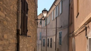 Une rue étroite bordée d’immeubles en pierre, avec un trottoir pavé et un lampadaire.