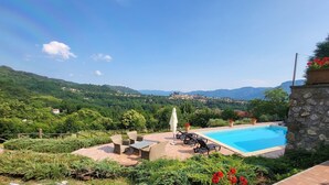 A pool area with outdoor furniture, a stone wall, and a view of a town and mountains in the background. - Casa Roc,  Private Pool, & Arguably Best View In Barga! WIFI. Walk to rest/bar (Barga)
