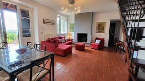 A living room with a red sofa, a glass dining table, and a fireplace. - Casa Roc,  Private Pool, & Arguably Best View In Barga! WIFI. Walk to rest/bar (Barga)
