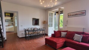 A spacious living area with a red sofa, a dining table set for four, and a kitchen in the background. - Casa Roc,  Private Pool, & Arguably Best View In Barga! WIFI. Walk to rest/bar (Barga)