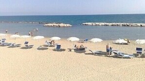 Een strand met ligbedden en parasols, rotsformaties in het water, en heldere luchten.