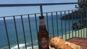 Een tafel met een fles Peroni bier, een brood en een bord eten met tomaten en kaas, met uitzicht op de oceaan.