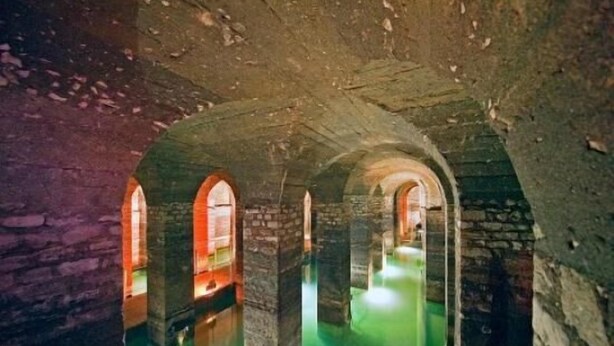 Een interieur met stenen bogen en een vloer in groen licht.