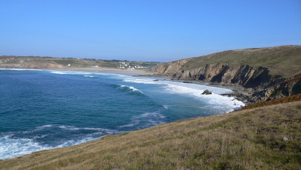 A coastal landscape with a grassy hill, ocean waves, and distant houses. - Character house where one is at home (Plouhinec)