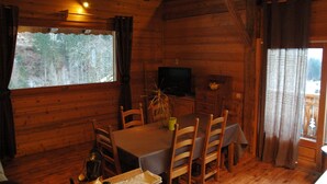 A wooden cabin interior with a dining table, chairs, a television, and a window with a view of trees. - Apartment in a chalet of character with ski access (Montriond)