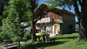 A rustic wooden building with a stone foundation, a balcony, and a small garden area with a bench and table. - Apartment in a chalet of character with ski access (Montriond)
