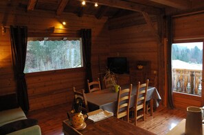 A wooden cabin interior with a dining table, chairs, a television, and a window with a view of trees. - Apartment in a chalet of character with ski access (Montriond)