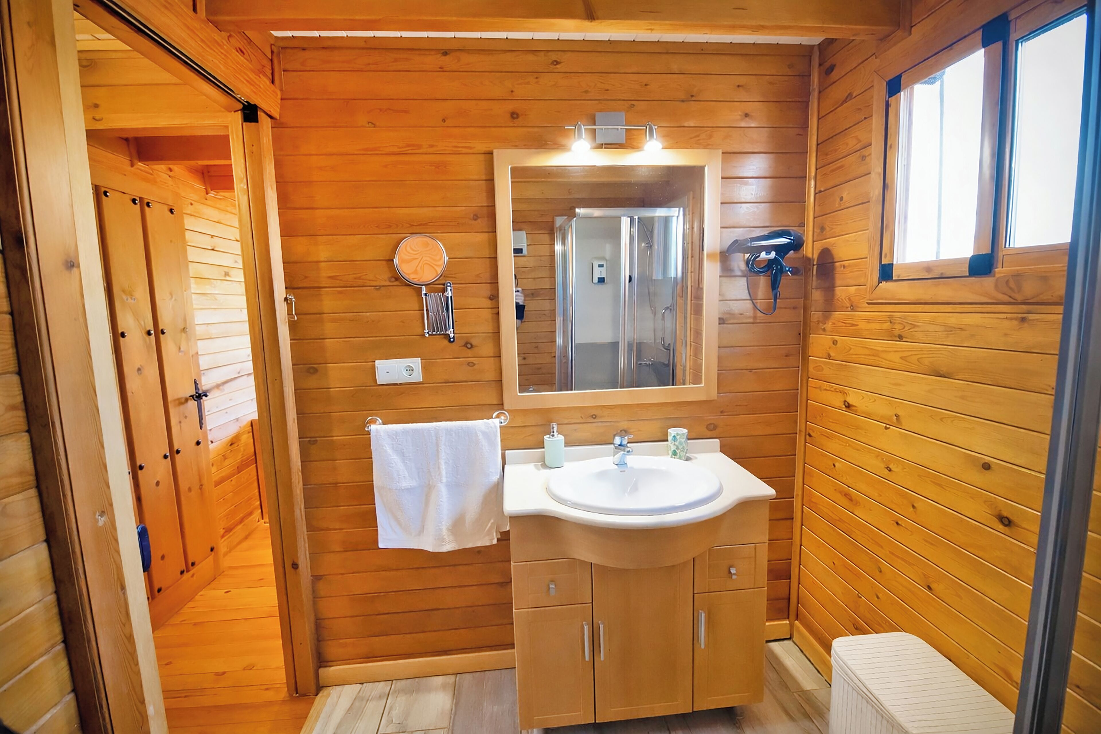 A wooden cabin bathroom with a sink, mirror, towel, and shower.