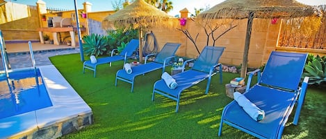 Un área junto a la piscina con sillones de descanso, una piscina pequeña y una estructura de techo de paja.