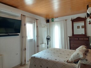 Ein Schlafzimmer mit Bett, Kommode, Spiegel, Fernseher und Deckenventilator.