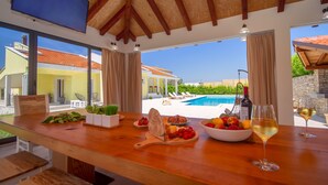 Eine Holzbar mit Blick auf einen Pool, eine Weinflasche und eine Obstschale.