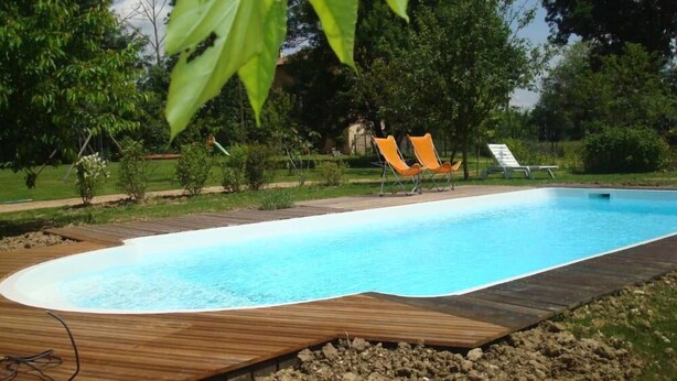 Une piscine dont les bords sont recouverts de bois, entourée d’un jardin aménagé avec des arbres et des arbustes.