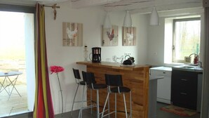 Une cuisine compacte avec un îlot central en bois, des tabourets de bar, une machine à café et un évier.