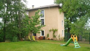 Une maison avec un patio, un espace de jeux doté d’un toboggan et une pelouse.