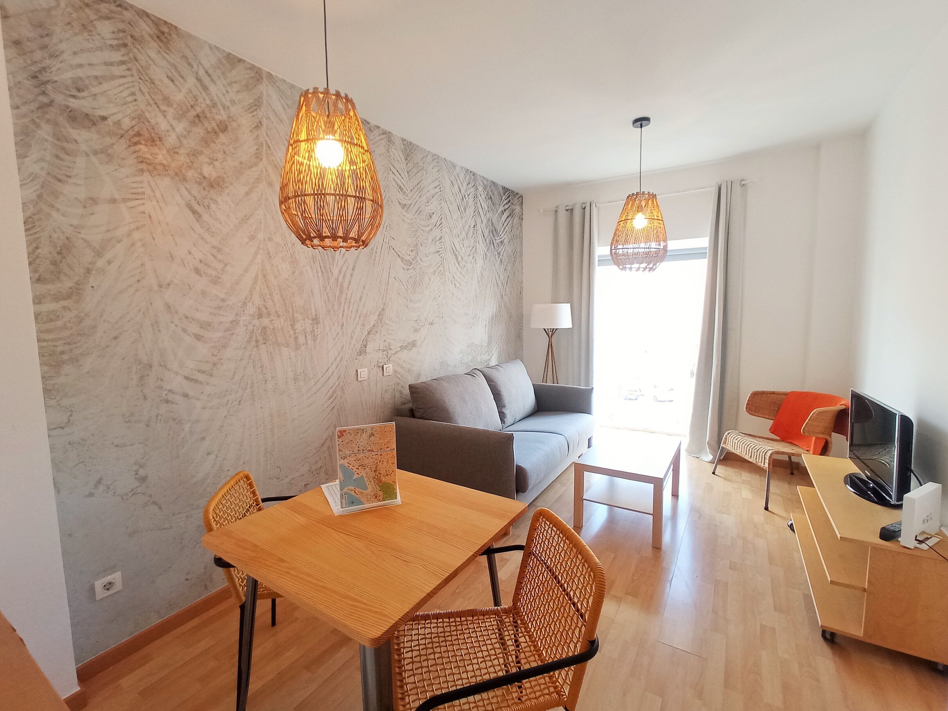 A modern living room with a sofa, dining table, wicker chairs, and a TV.