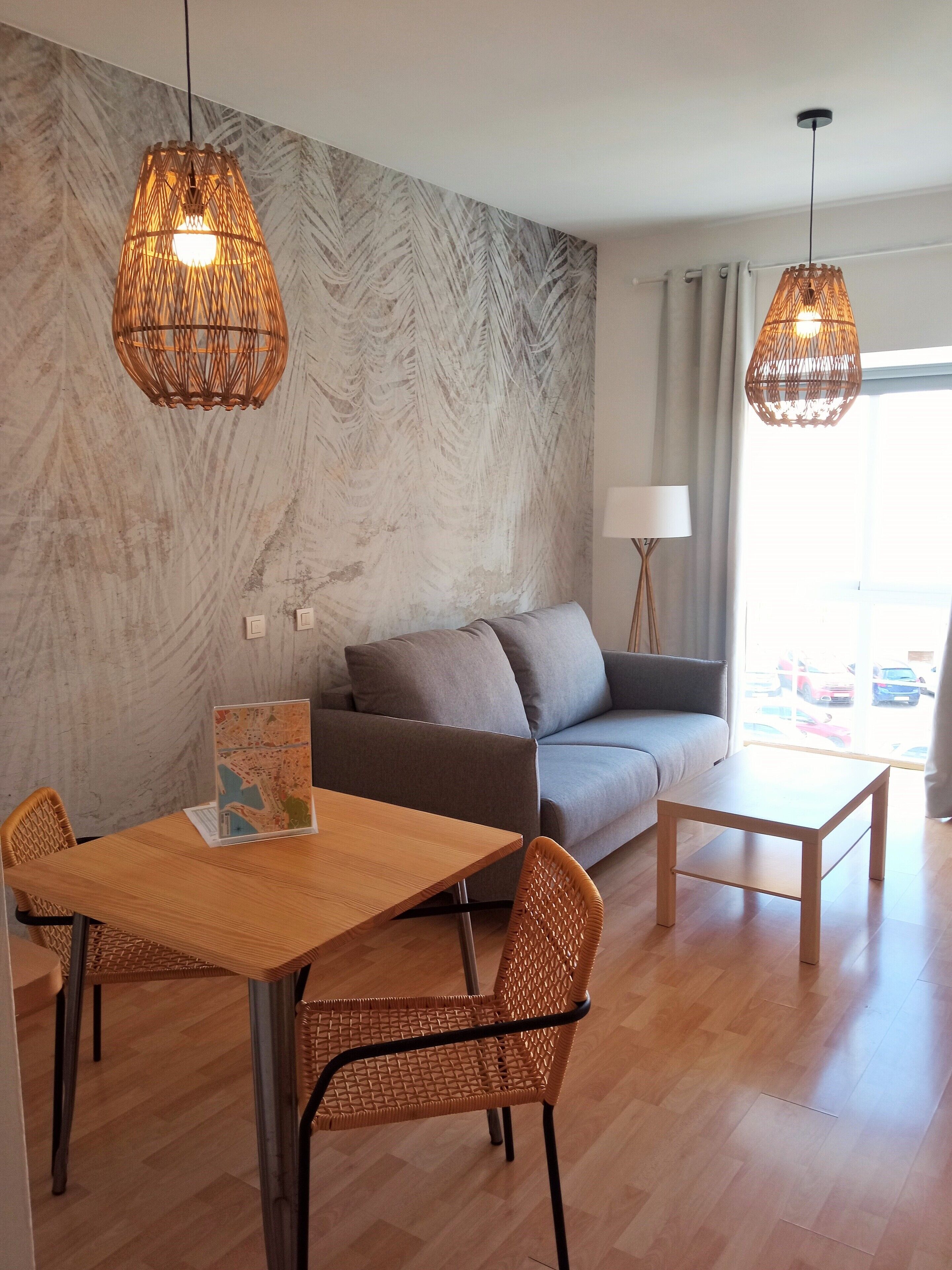 Een moderne woonkamer met een bank, een eettafel met stoelen en twee hangende rieten lampen.