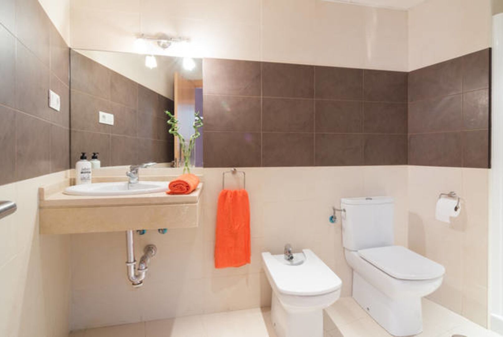 Un baño moderno con un lavamanos, dos inodoros y un espejo.