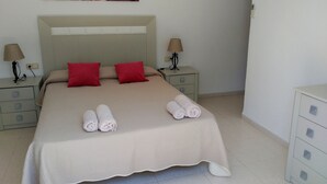 Una cama bien hecha con almohadas rojas, dos lámparas de noche y toallas enrolladas sobre la cama.