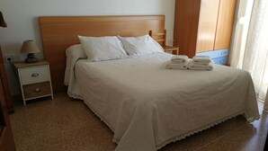 A neatly made bed with white linens, a wooden headboard, and a nightstand with a lamp and a drawer.