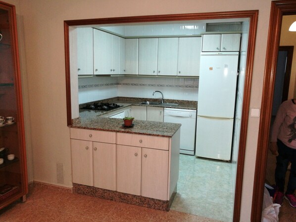 Una cocina compacta con armarios blancos, encimera de granito, estufa, lavaplatos y lavavajillas.