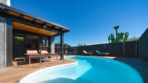 A modern outdoor pool area with wooden decking, lounge chairs, and a covered seating area.
