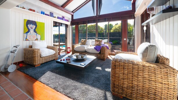 A sunlit room with wicker furniture, a painting on the wall, and a skylight.