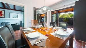 A dining area with a wooden table set for six, surrounded by chairs, with a view of the outdoors through large windows.