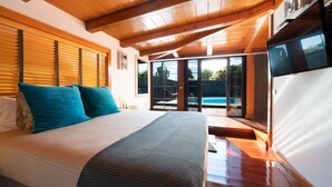 A bedroom with a large bed, wooden ceiling, and a sliding glass door leading to a pool area.