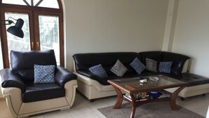 A living room with a black leather sofa, a beige armchair, and a glass coffee table with books and a remote control. - 5 Star Luxury Villa - Large Private Pool - Spacious Rooms - Panoramic Sea Views (Balchik/Albena, Black Sea Coast)