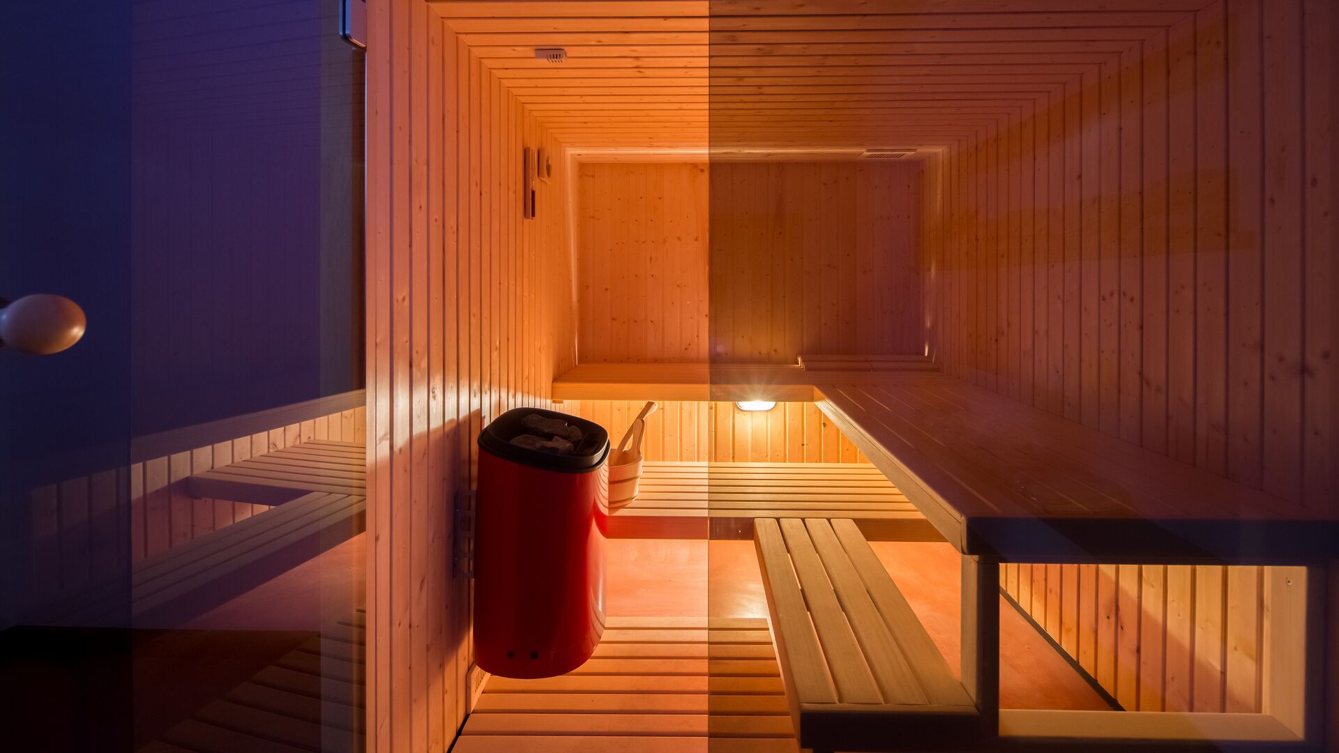 A sauna with wooden walls and benches, a red container, and a small table.