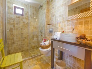 Een badkamer met een douchecabine van glas, een gele stoel, een toilet, een wastafel met spiegel en een mand met handdoeken.