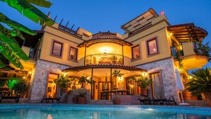 Ein zweigeschossiges Haus mit Swimmingpool, Sitzgelegenheit im Freien und Topfpflanzen.