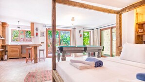Ein Zimmer mit einem Bett, einem Billardtisch, einem Holztisch und einem Fenster mit Blick auf Grünfläche.