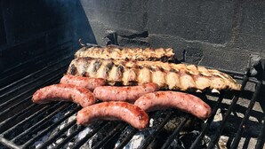 Una parrilla con salchichas y pollo asándose.