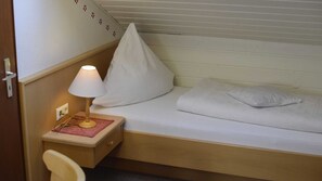 Une petite chambre avec un lit simple, une table de chevet, une lampe et une chaise.