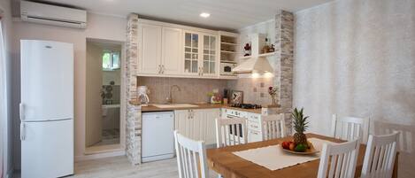 Una cocina compacta con muebles blancos, una mesa de comedor de madera y un horno empotrado.