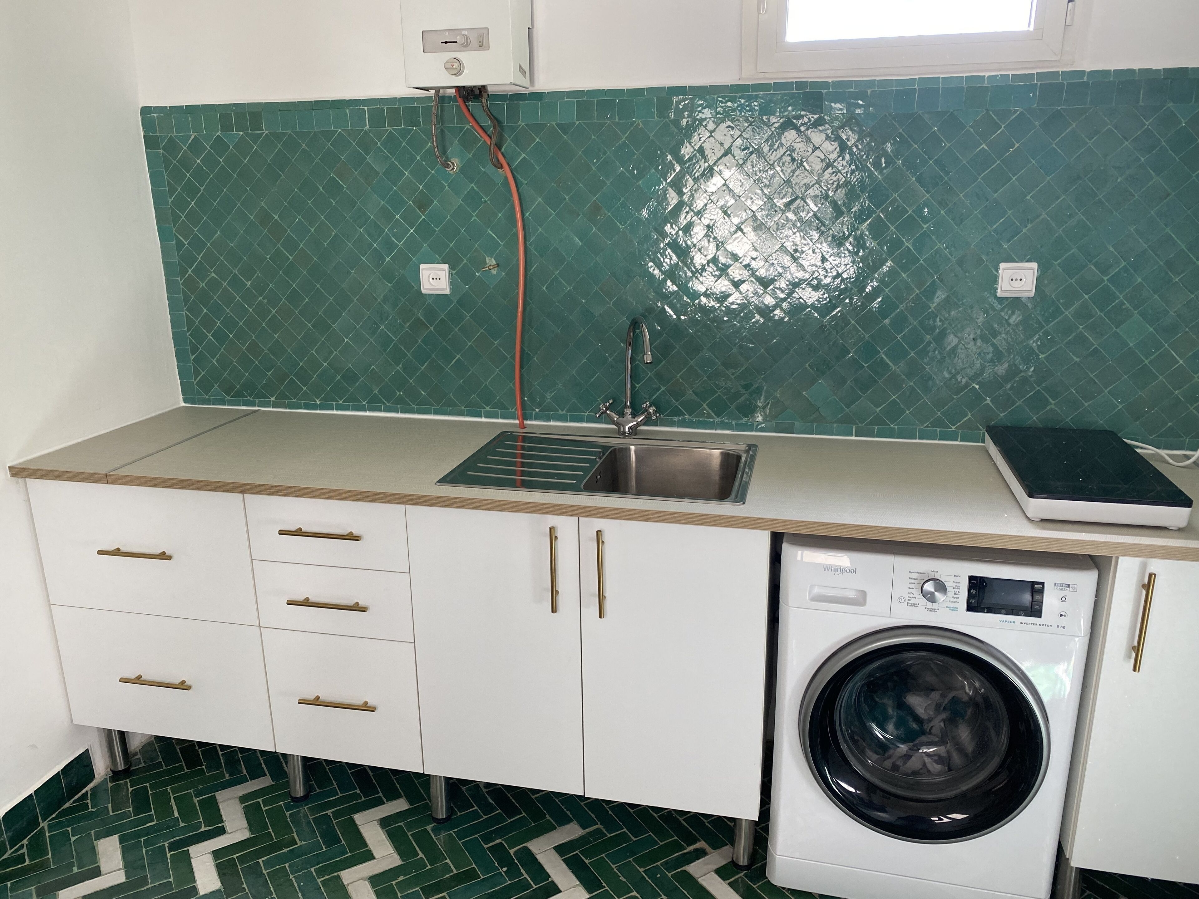 A compact kitchen with a washing machine, a sink, and a window above the sink.