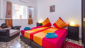 A bedroom with a bed, a sofa, a nightstand, a lamp, and a window with curtains. - Marrakech's Historic Heart – Palace Quarter in the Medina (Marrakesch)