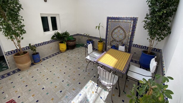 A small patio area with a tiled floor, a table with a yellow tablecloth, a chair, and several potted plants. - Marrakech's Historic Heart – Palace Quarter in the Medina (Marrakesch)