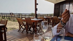 An outdoor dining area with wooden tables and chairs, a wooden deck, and a view of the beach. - Beachfront house, Manta Rota, Algarve (Private pool, Outdoor BBQ, Free Wifi, AC ..) (Vila Nova de Cacela)
