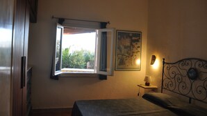 A bedroom with a bed, a window, a wall-mounted picture, and a bedside table with a lamp. - GARDEN VILLA DOLPHIN SEASIDE (Golfo Aranci)