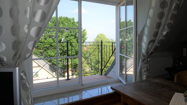 A room with a large window, a wooden table, and a wicker chair. - Apartment with flair in the south of Dresden (Plauen)