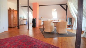 A spacious living area with a large wooden floor, a red patterned rug, wicker chairs, a dining table, and a kitchen in the background. - Apartment with flair in the south of Dresden (Plauen)