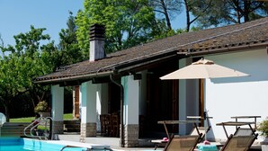 A poolside area with lounge chairs and a table, a covered patio, and a clear view of the pool.