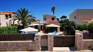 A residential area with stone walls, a wooden gate, and a pool area with lounge chairs and umbrellas.