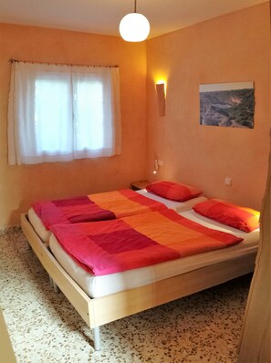 A bedroom with a bed, a window with curtains, a wall-mounted light, and a landscape painting.